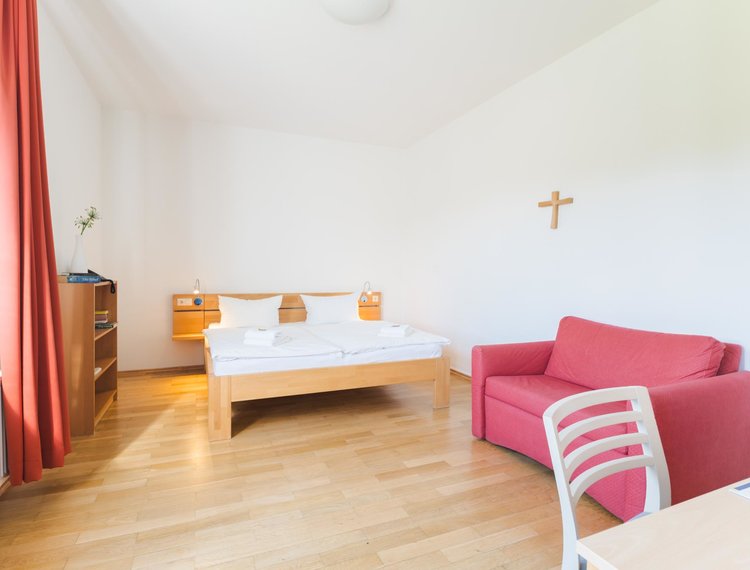 Ein Doppelbett und ein rotes Sofa stehen in einem Raum