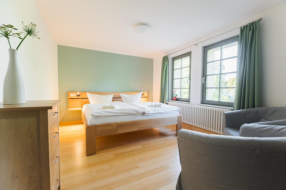 Ein Doppelbett und zwei Sessel stehen in einem Raum mit einer grünen Wand und grünen Gardinen