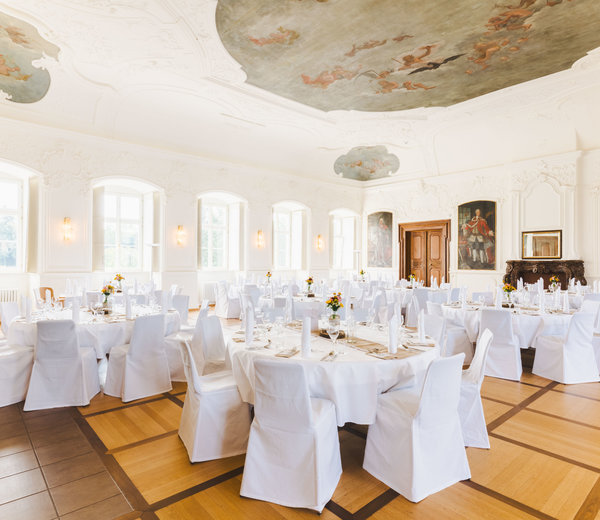 Der große Kaisersaal ist feierlich geschmückt. Die runden Tische sind mit weißen Tischdecken gedeckt und die Stühle in weißen Stoffen gehüllt. Die Tische sind gedeckt mit Besteck, weißen Servietten und einer Blumenvase